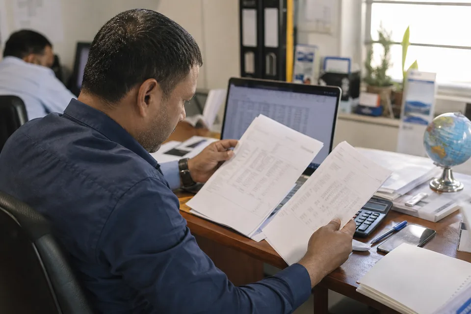 Person reviewing printed documents beside a laptop and calculator