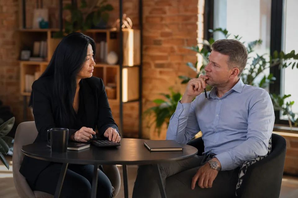 A sales manager and a founder discussing a software budget across a small meeting table