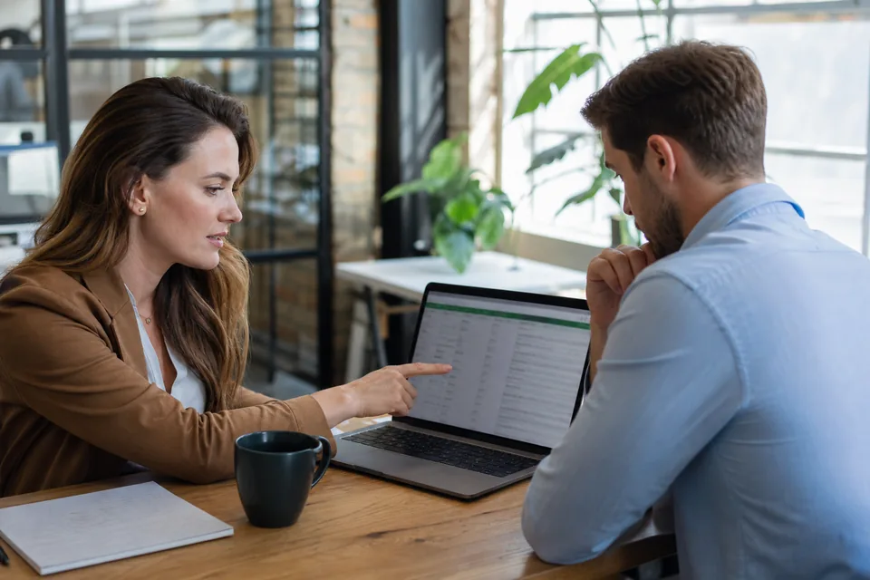 A recruiter and a sales rep checking a contact spreadsheet on a laptop in a bright office